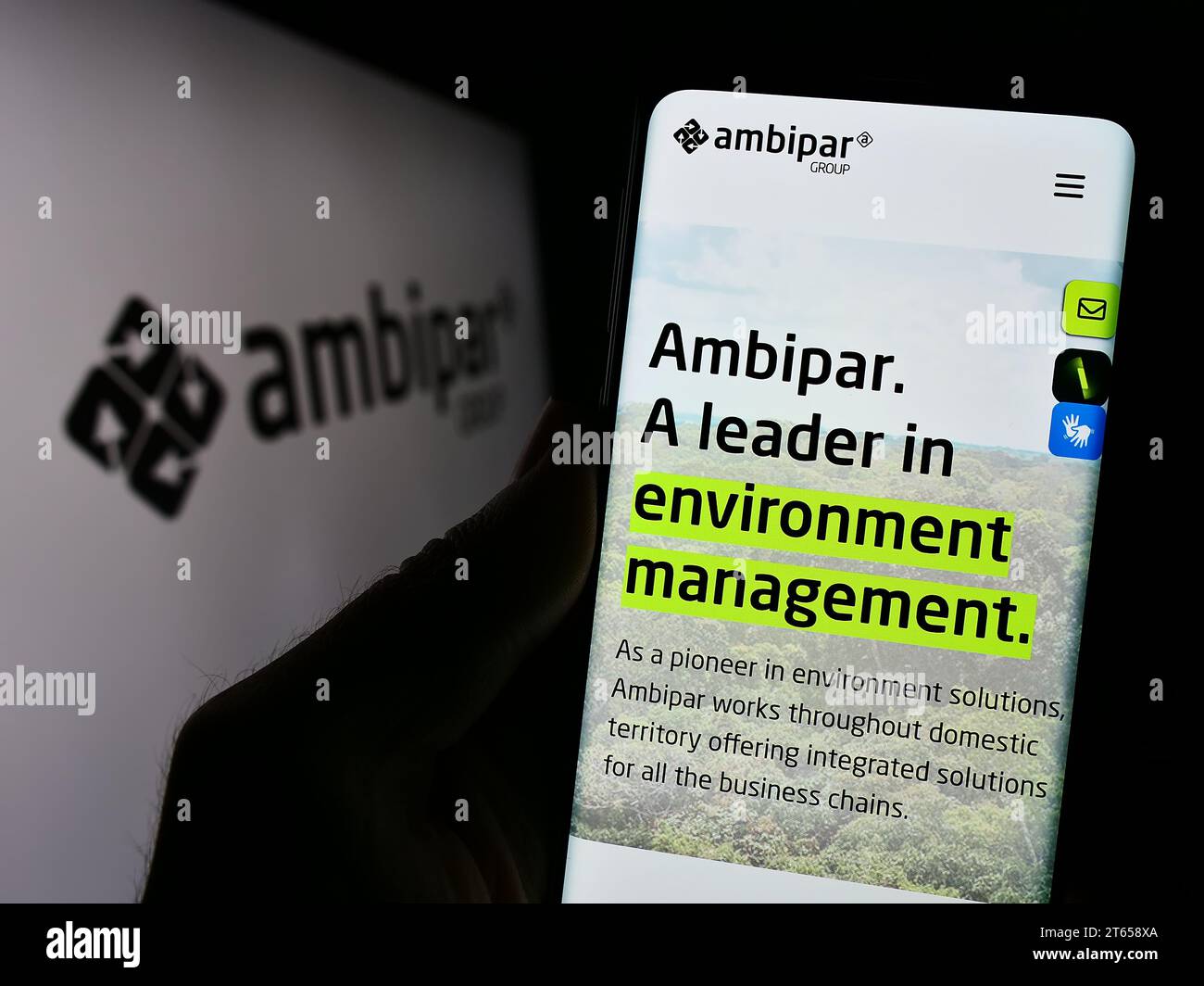 Person holding cellphone with webpage of Brazilian environmental services company Ambipar Group with logo. Focus on center of phone display. Stock Photo