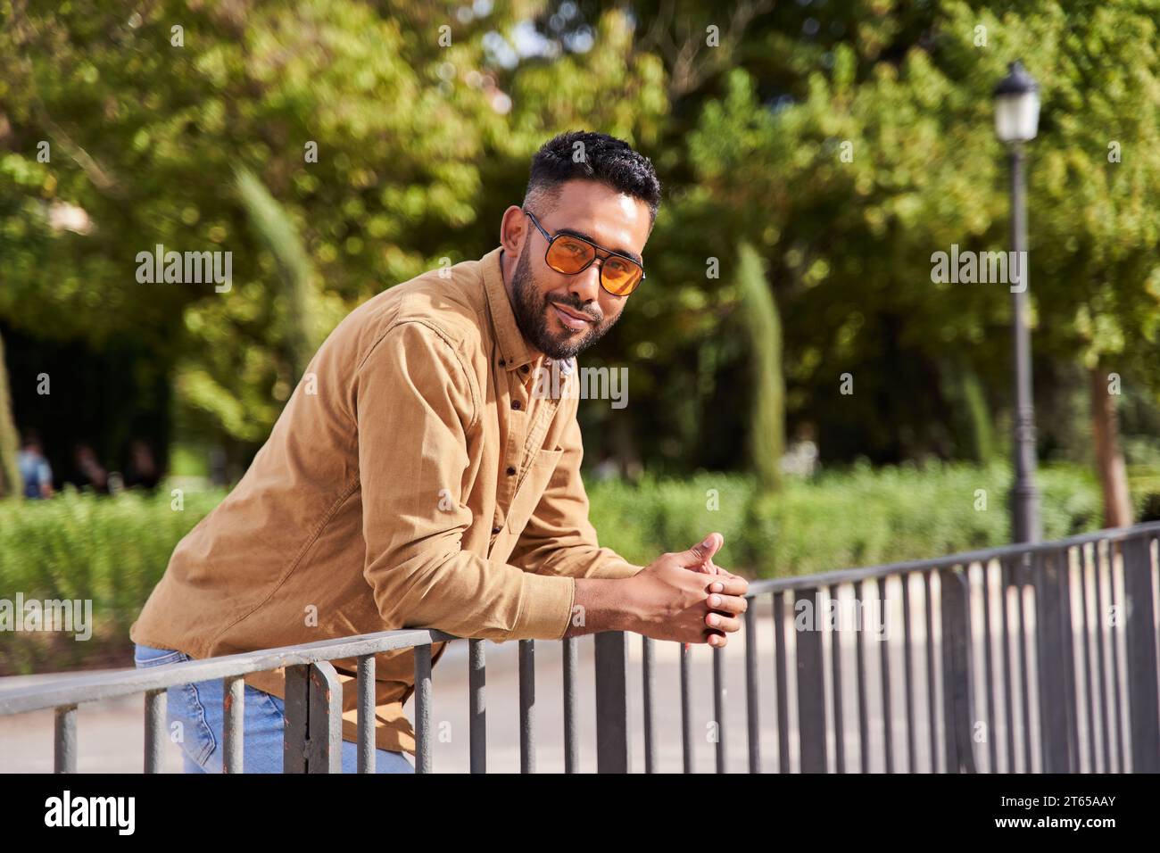latin man leaning on railing looking at camera with orange sunglasses and casual clothing Stock Photo