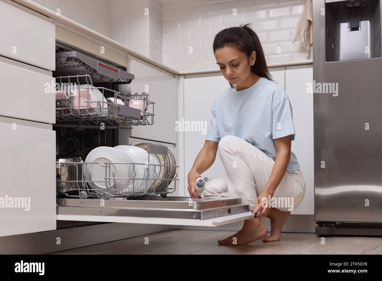 woman pours rinse aid into the dishwasher compartment in modern white
