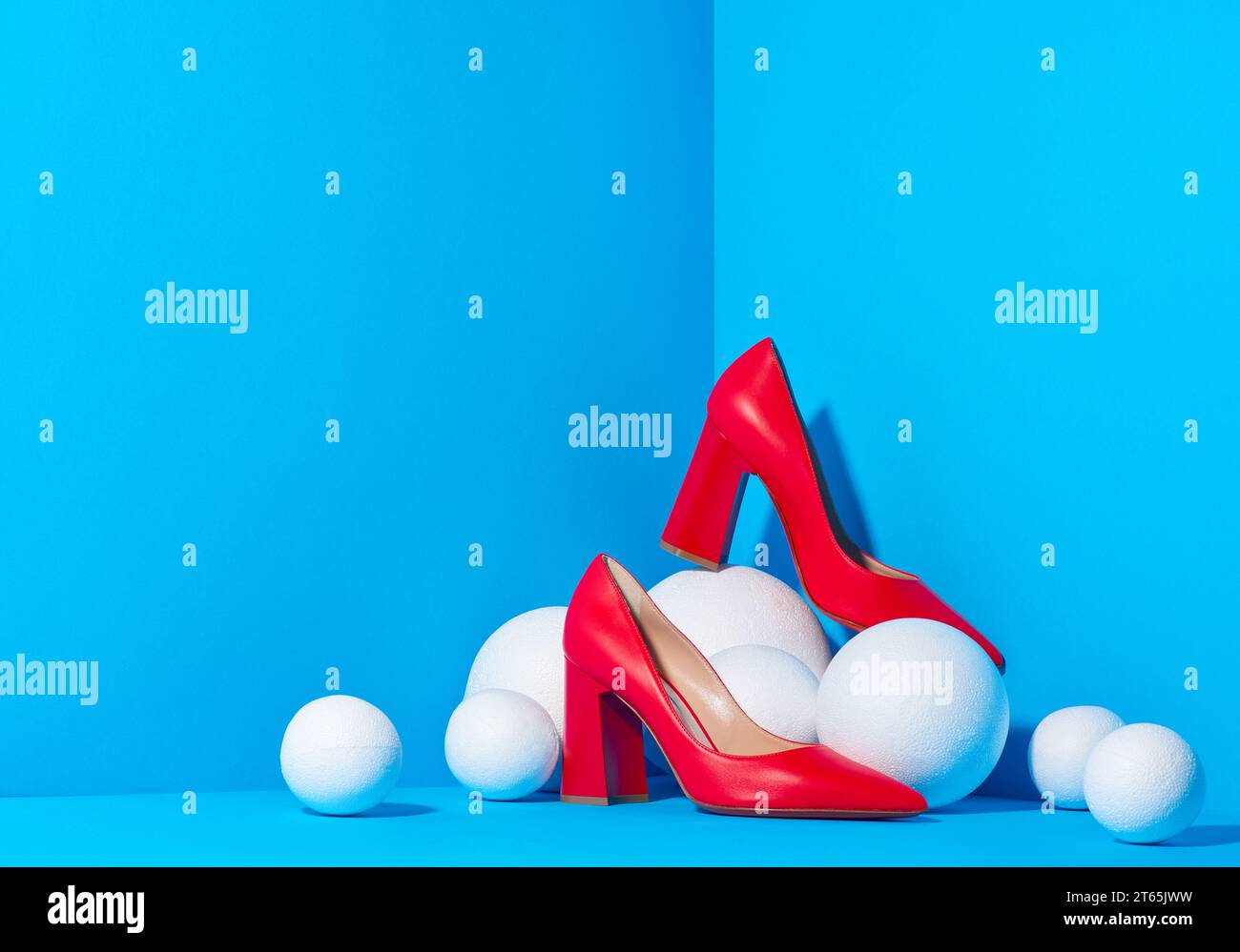Stylish fashion female red high-heeled shoes are placed in a cube with a blue solid background and white balls around that resemble snowballs. There i Stock Photo