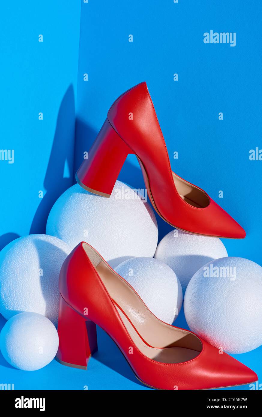 Ffashionable female red high-heeled shoes on a blue solid background lie on white balls around that resemble snowballs. Winter concept. Fashion blog l Stock Photo