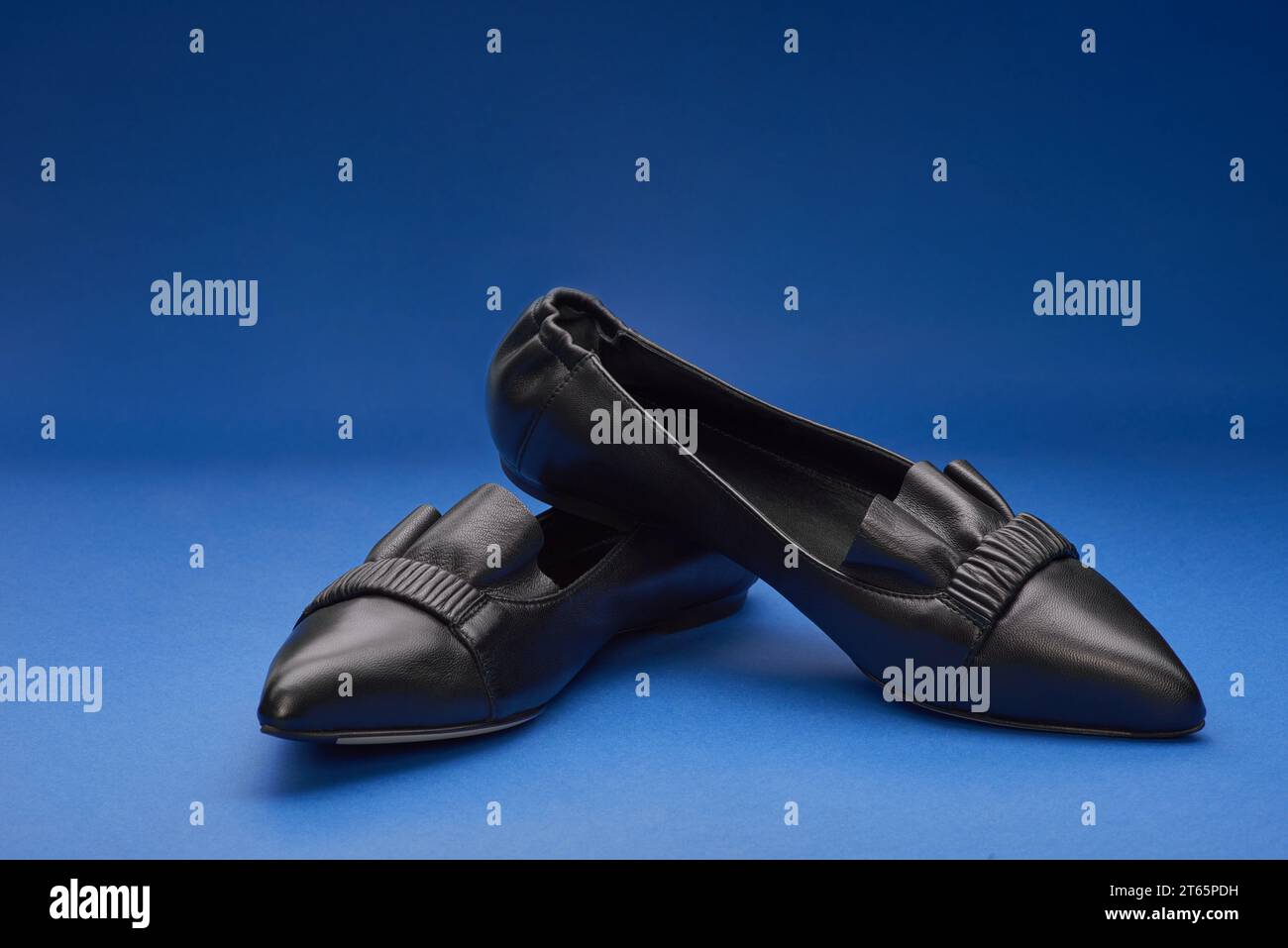 Elegant black pointed-toe leather ballet flats with wrinkled and ruffle details on the blue gradient background. Copy space. Creative minimalistic lay Stock Photo