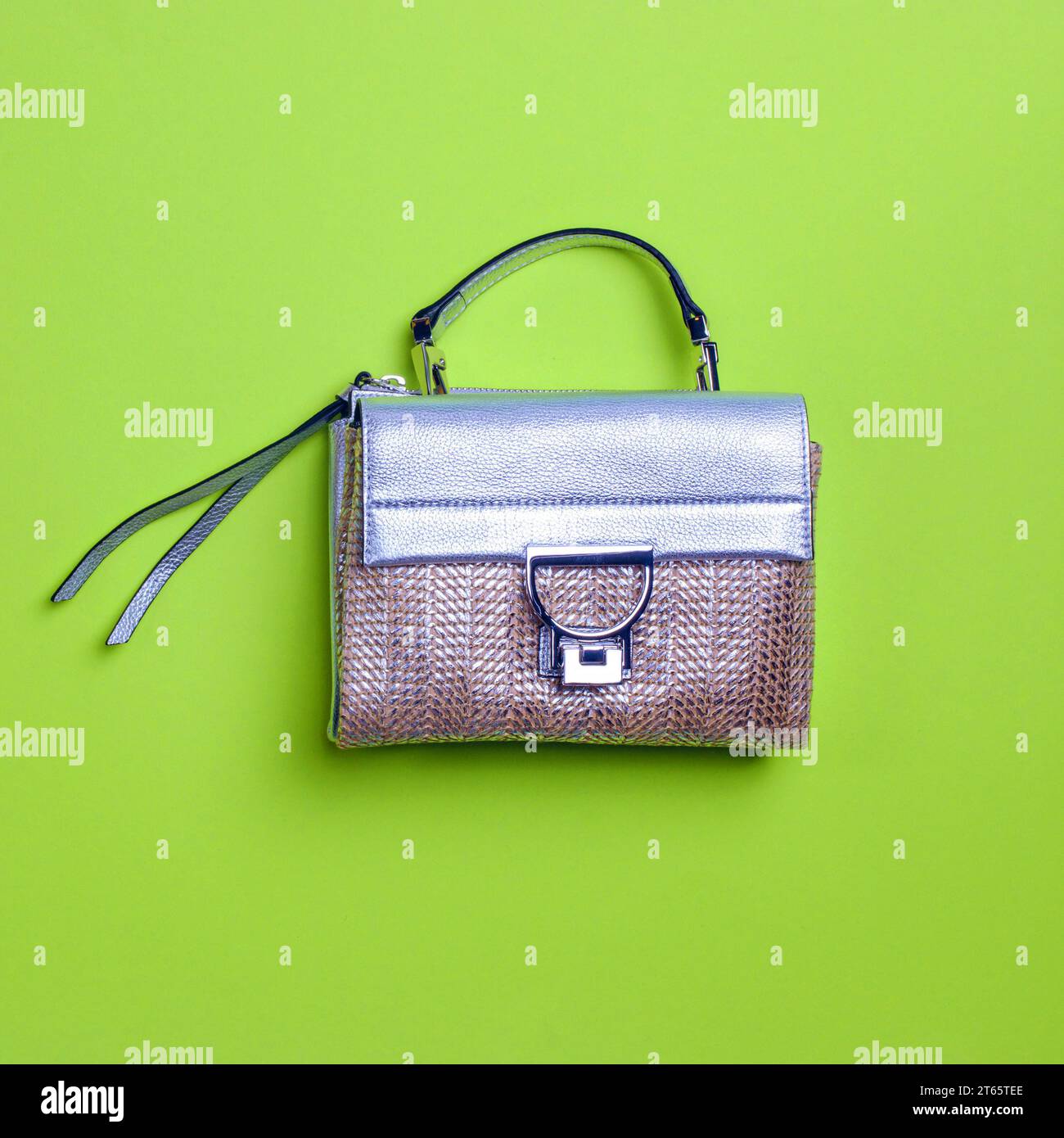 Bold woven design female handbag with silver leather flap, top handle, and zipper pull isolated on a green background with copy space. Creative design Stock Photo
