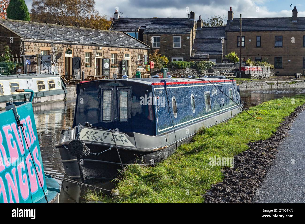 A barge (narrowboat, flat bottomed boat) is moored up on the Leeds Liverpool canal in Bingley, Yorkshire. Five Rise Locks cafe is in the background. Stock Photo