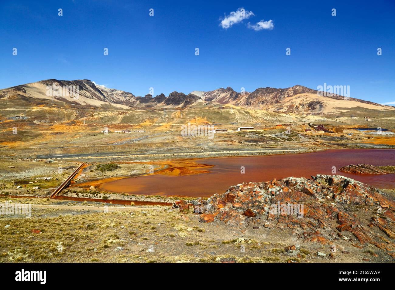 View across lake and aqueduct contaminated by acid mine drainage and industrial waste from the nearby tin mine at Milluni (part of which can be seen on the far bank and mountainside), near La Paz, Bolivia. The mountains are the foothills of the Mt Chacaltaya massif. Stock Photo