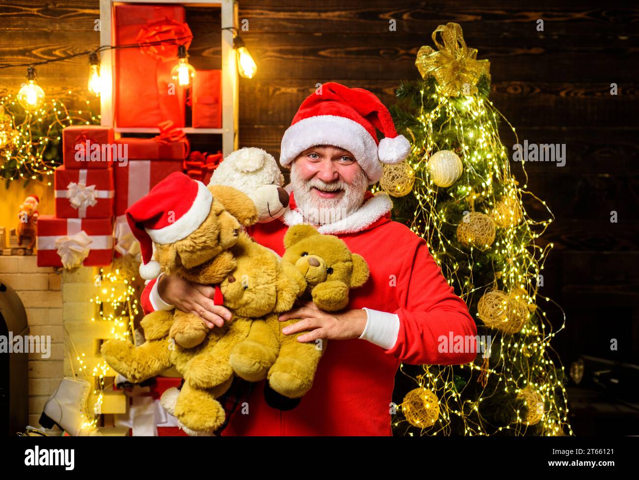 Christmas holidays. Smiling Santa Claus with many teddy bears. Bearded man in Santa hat with teddy bears in room decorated for Christmas. Santa man Stock Photo