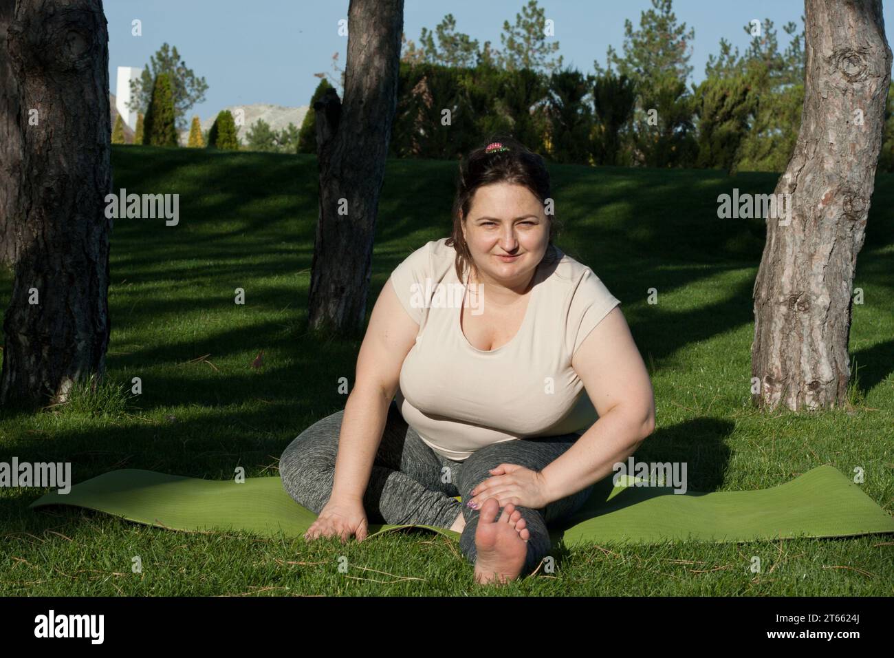 Beautiful fat woman doing yoga on the mat in the park Stock Photo