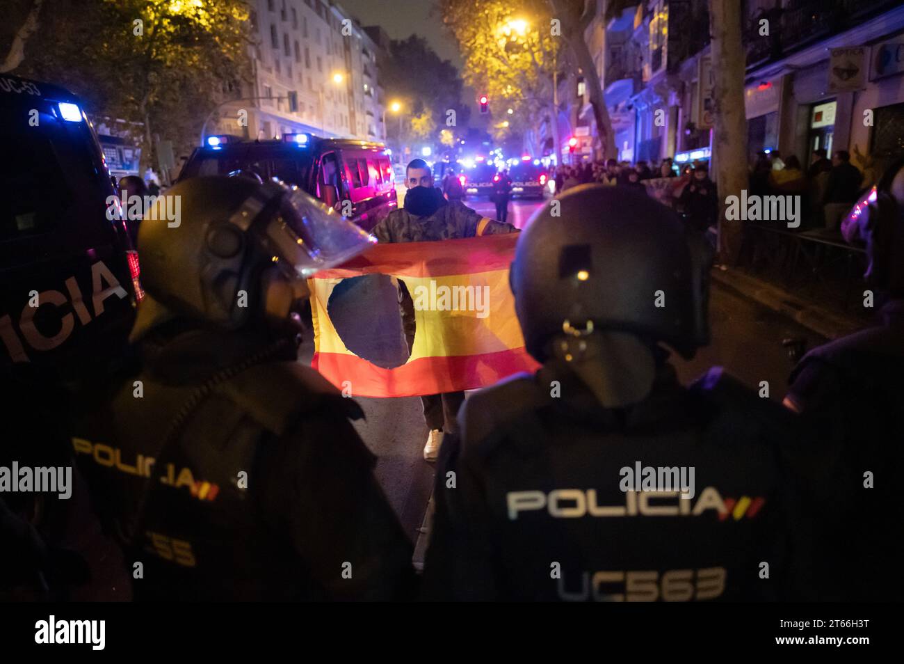 Madrid, Spain. 08th Nov, 2023. A demonstrator hods a Spanish flag with the coat of arms deliberately cut in front of riot police during a protest near the socialist party PSOE headquarters in Ferraz street. Thousands of people have gathered for another night to protest against the government of Pedro Sanchez and the possible approval of an amnesty for Catalan separatist leaders that the government is negotiating to guarantee the investiture of the socialist candidate. Credit: Marcos del Mazo/Alamy Live News Stock Photo