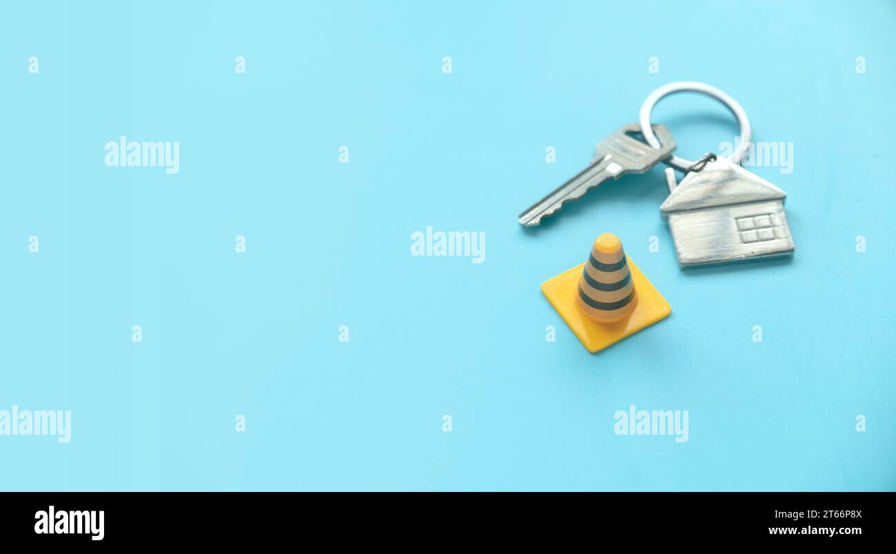 Concept of under construction or fixing for home, property or real estate.House key with traffic cone over a blue background with copy space. Stock Photo