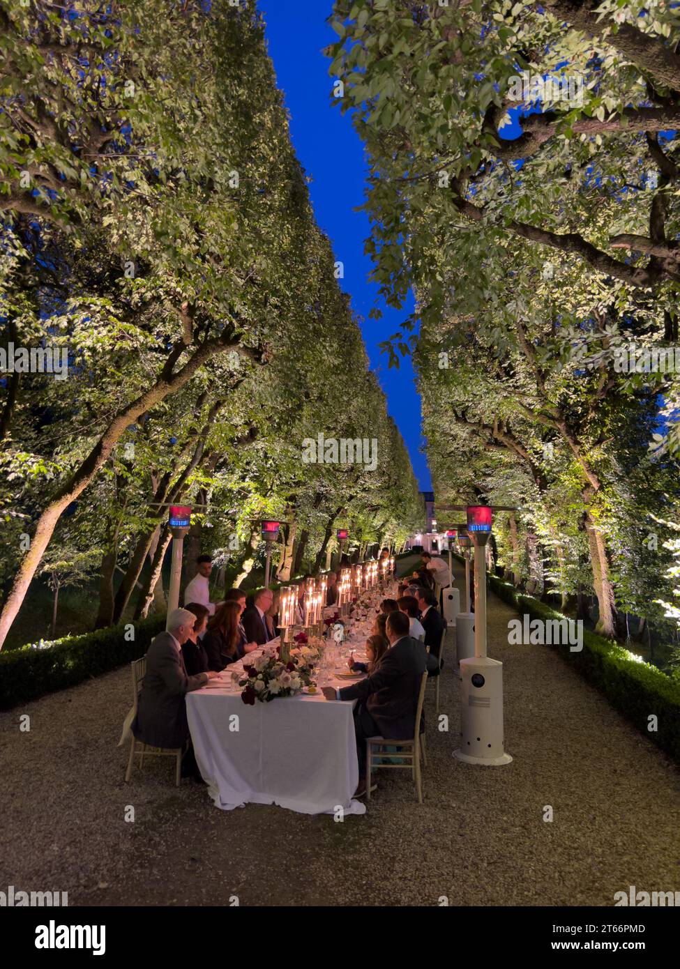Rome, Italy - 09 august 2023: Guests are sitting at the laid festive table on the alley in the garden near the outdoor gas heaters Stock Photo