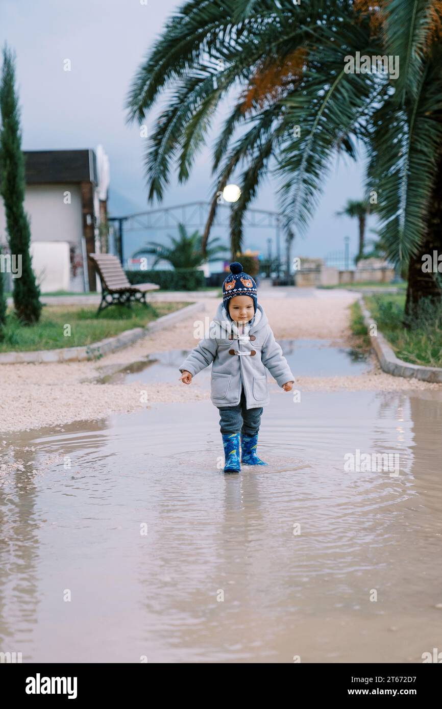 Little smiling girl in rubber boots walks through a puddle Stock Photo ...