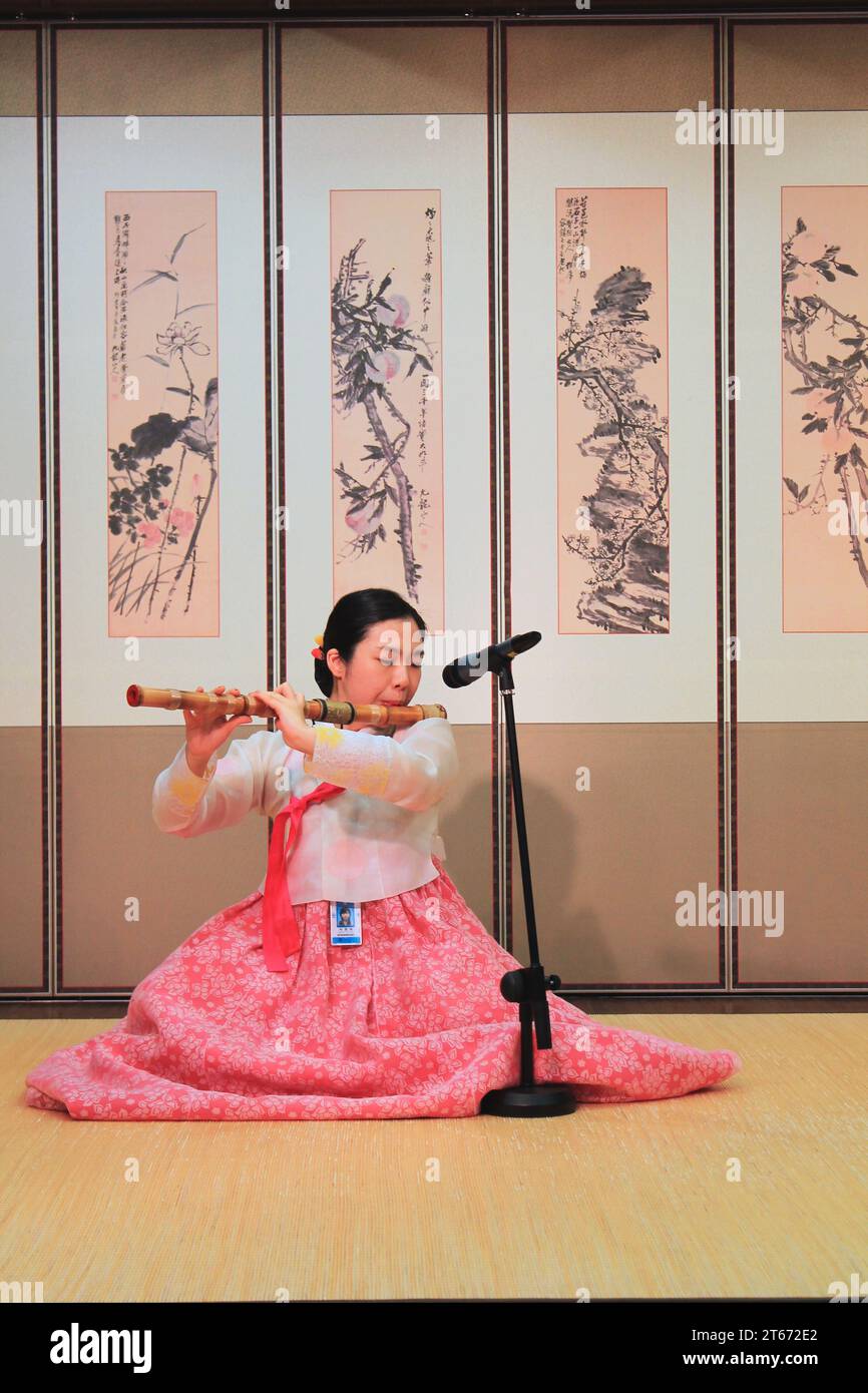 A Korean woman plays a traditional bamboo flute in front of several vintage ink drawings at the Korea Traditional Culture Experience Center in Incheon Stock Photo