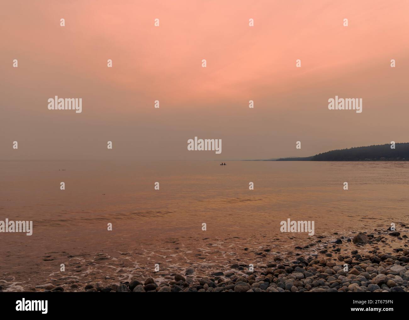 Smoky sunset on the Sunshine Coast in Canada, with the sun hidden by smoke from wildfires in British Columbia. Two people in a boat in the distance. Stock Photo