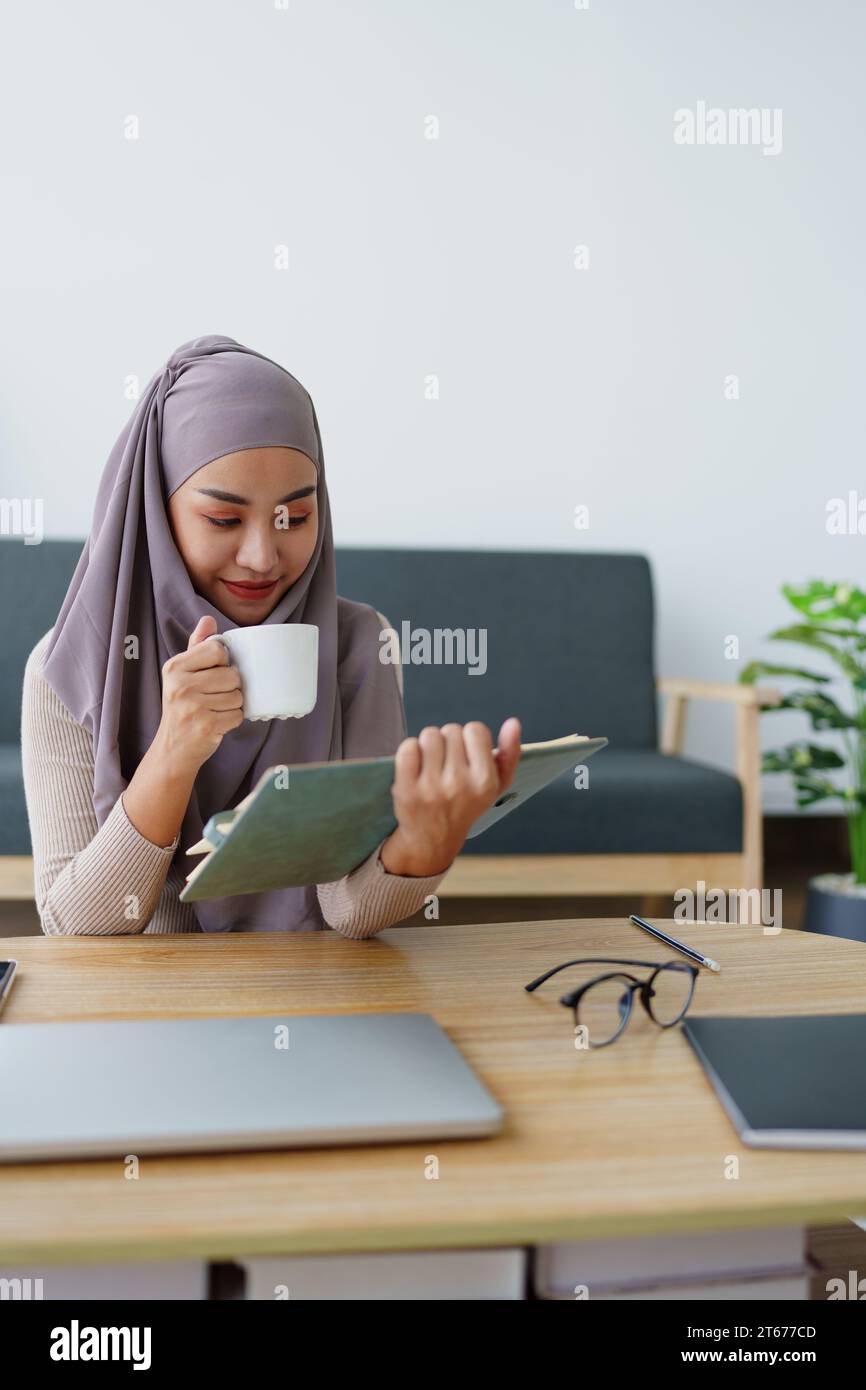 Muslim undergraduate student drinks coffee while read studying at home. Stock Photo