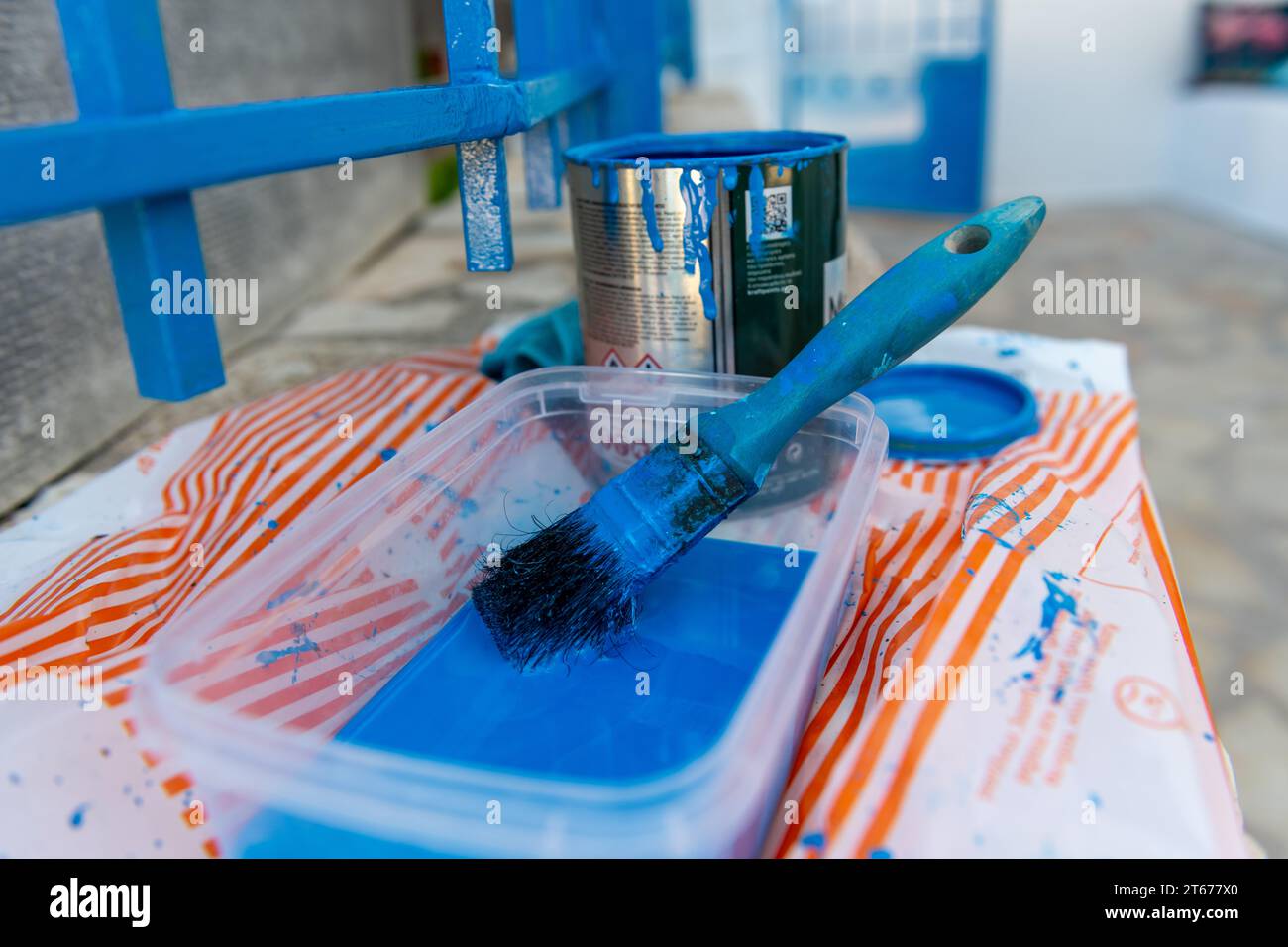 Painting a metal fence with a tin of blue paint and paint brush. Home