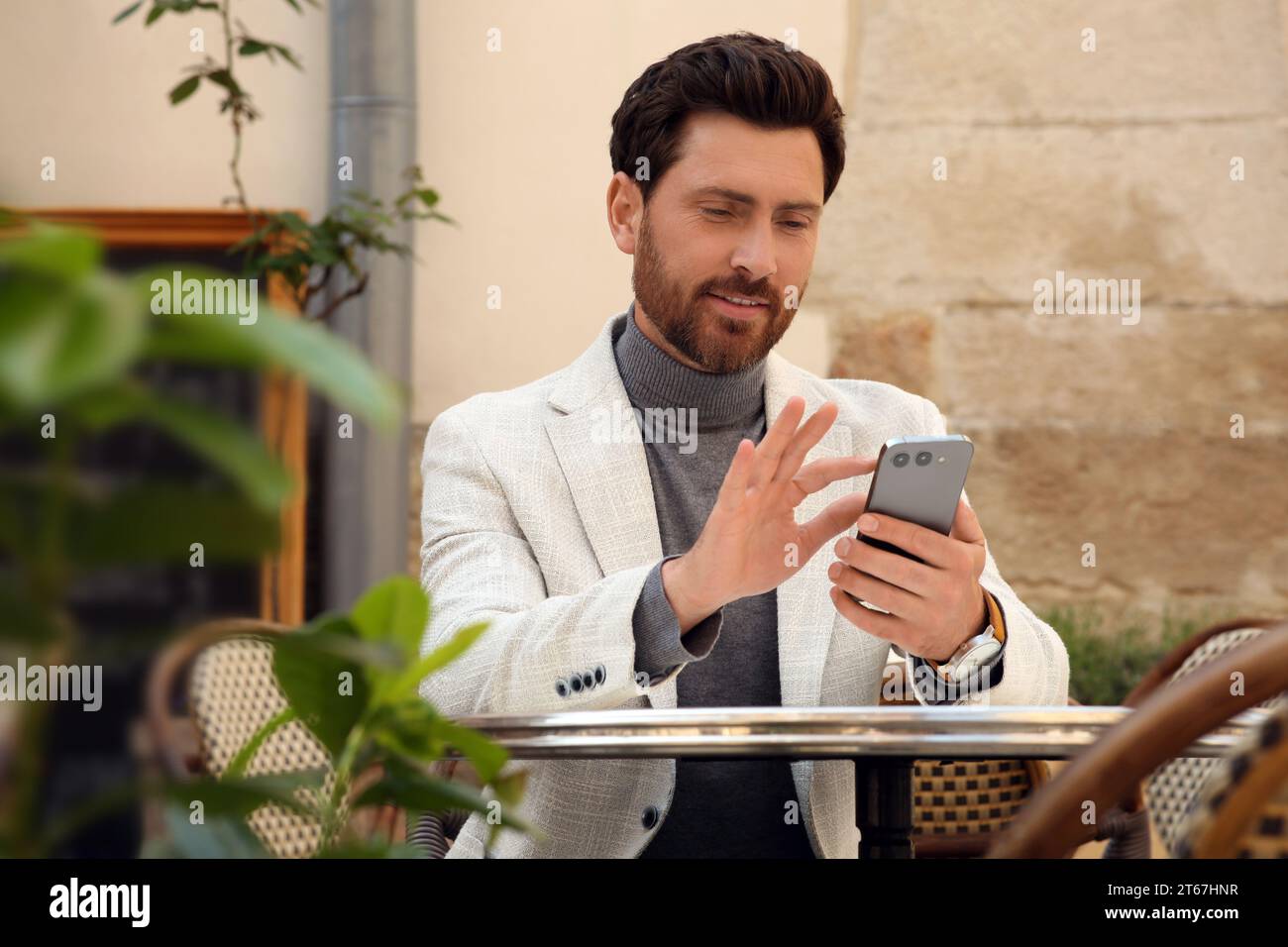 Handsome man sending message via smartphone at table outdoors Stock Photo