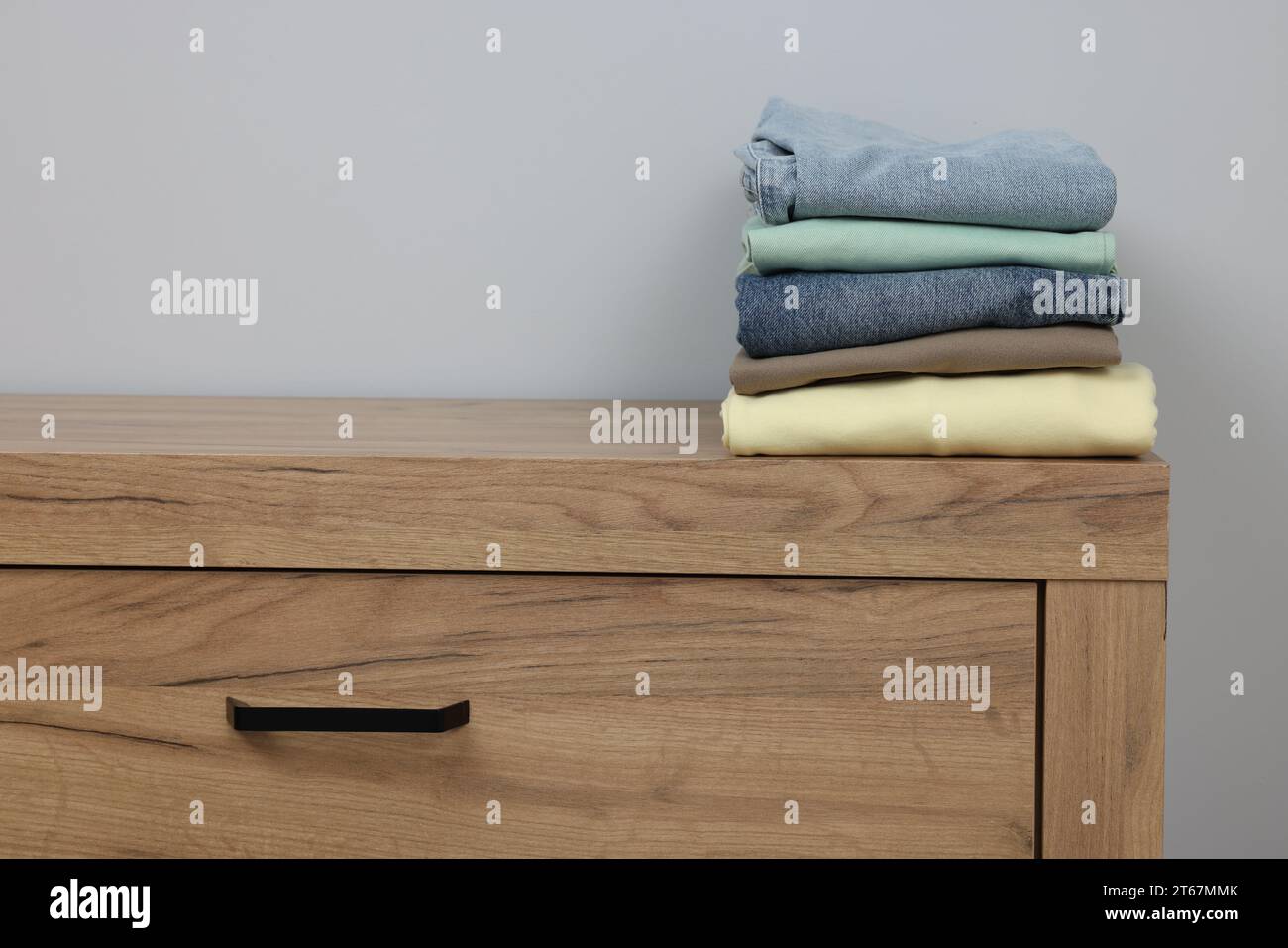 Different folded clothes on wooden chest of drawers near grey wall ...