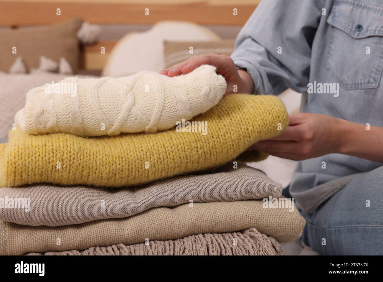 Woman with stack of different folded blankets and clothes on bed, closeup. Home textile Stock Photo