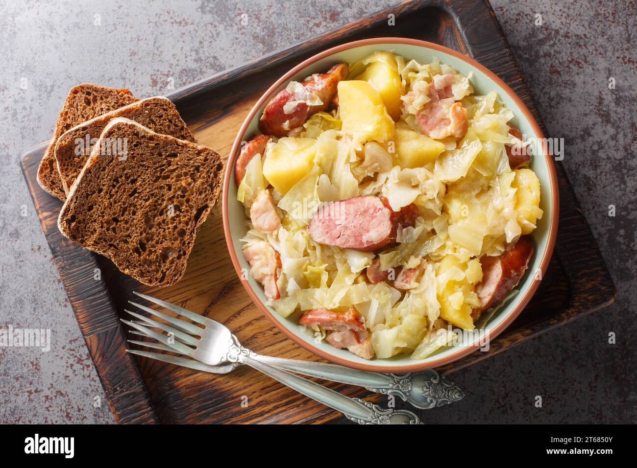 Cabbage stewed with potatoes, sausage, bacon and onions close-up in a bowl on the table. Horizontal top view from above Stock Photo