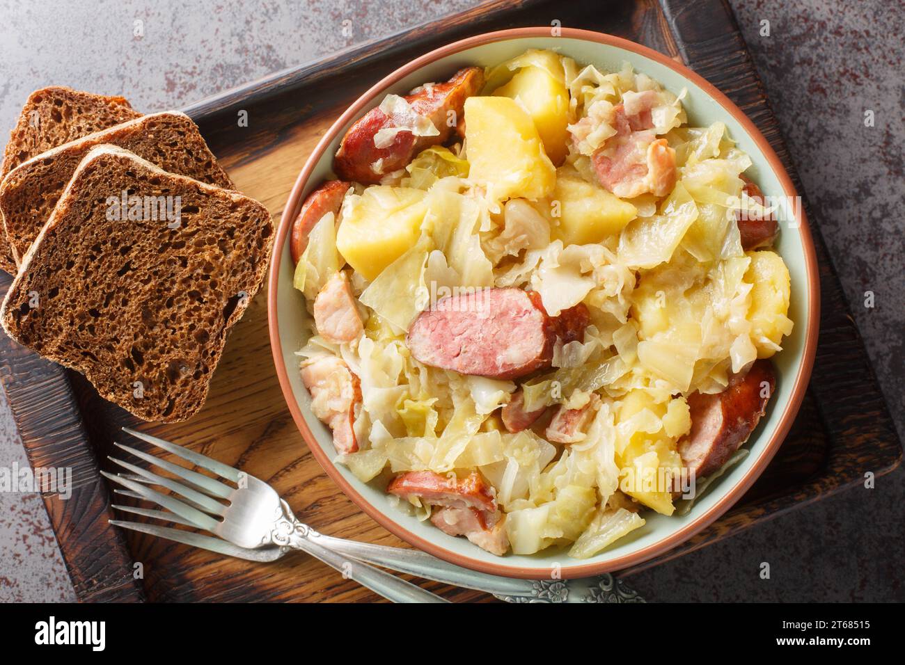 Hunter's cabbage stewed with sausage, potatoes, bacon and onions close-up in a bowl on the table. Horizontal top view from above Stock Photo