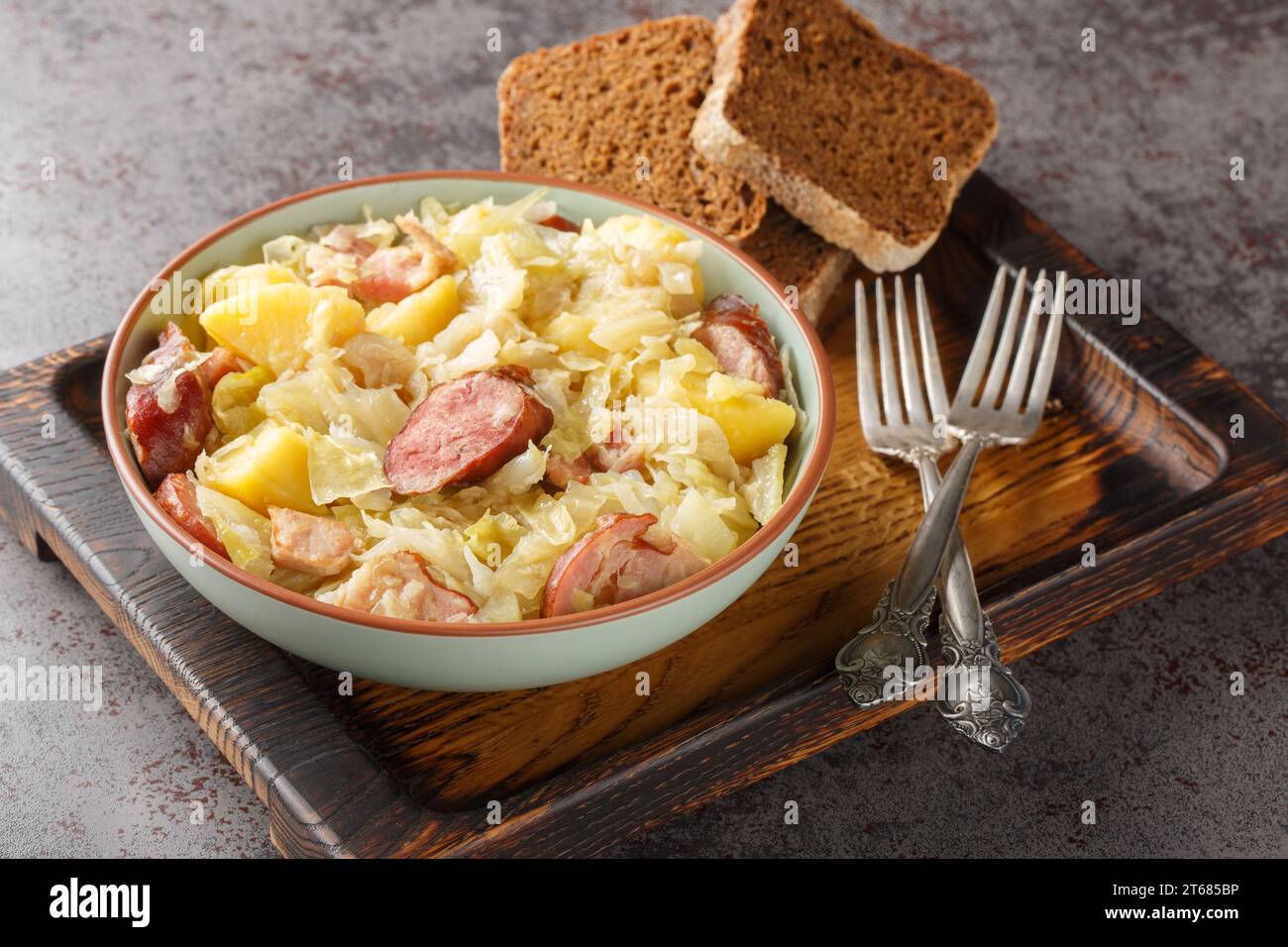 Cabbage stewed with potatoes, sausage, bacon and onions close-up in a bowl on the table. Horizontal Stock Photo