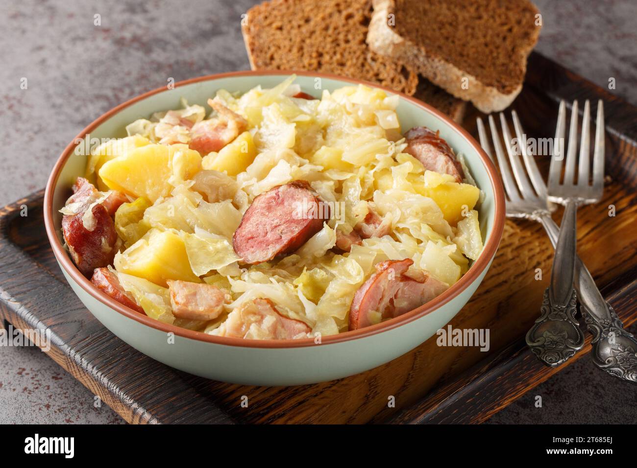 Hunter's cabbage stewed with sausage, potatoes, bacon and onions close-up in a bowl on the table. Horizontal Stock Photo