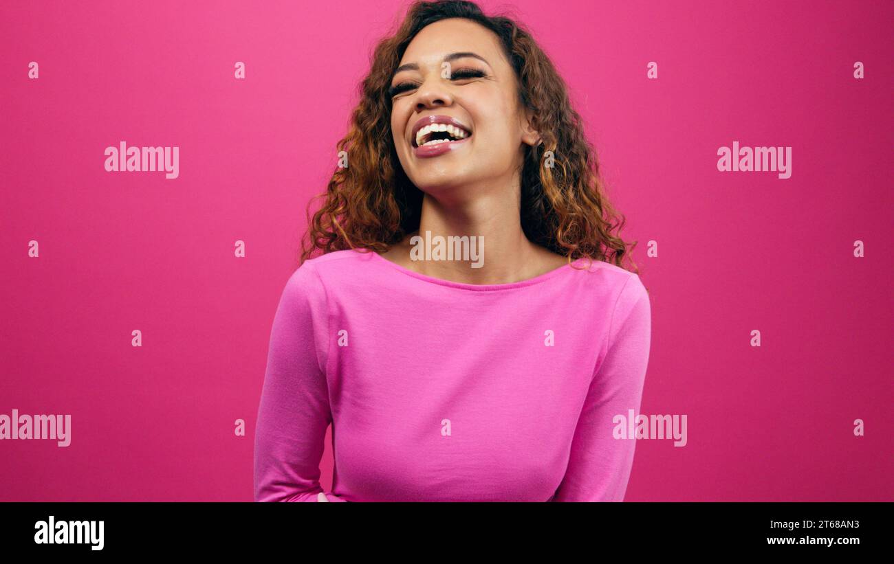 Happy young woman laughing in pink studio, wearing pink for Valentine's Day Stock Photo
