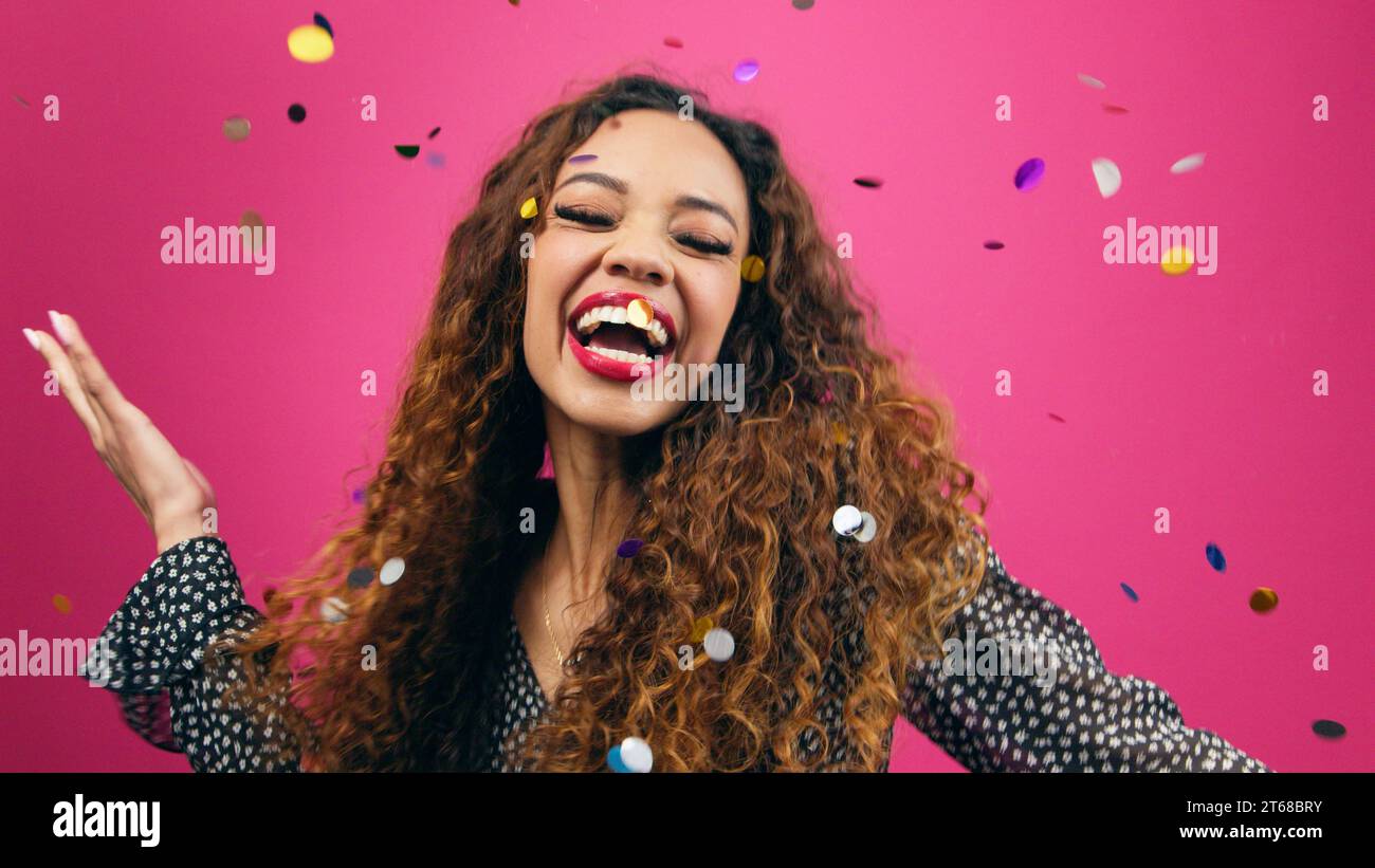Beautiful young woman dances while multi-coloured confetti rains down Stock Photo