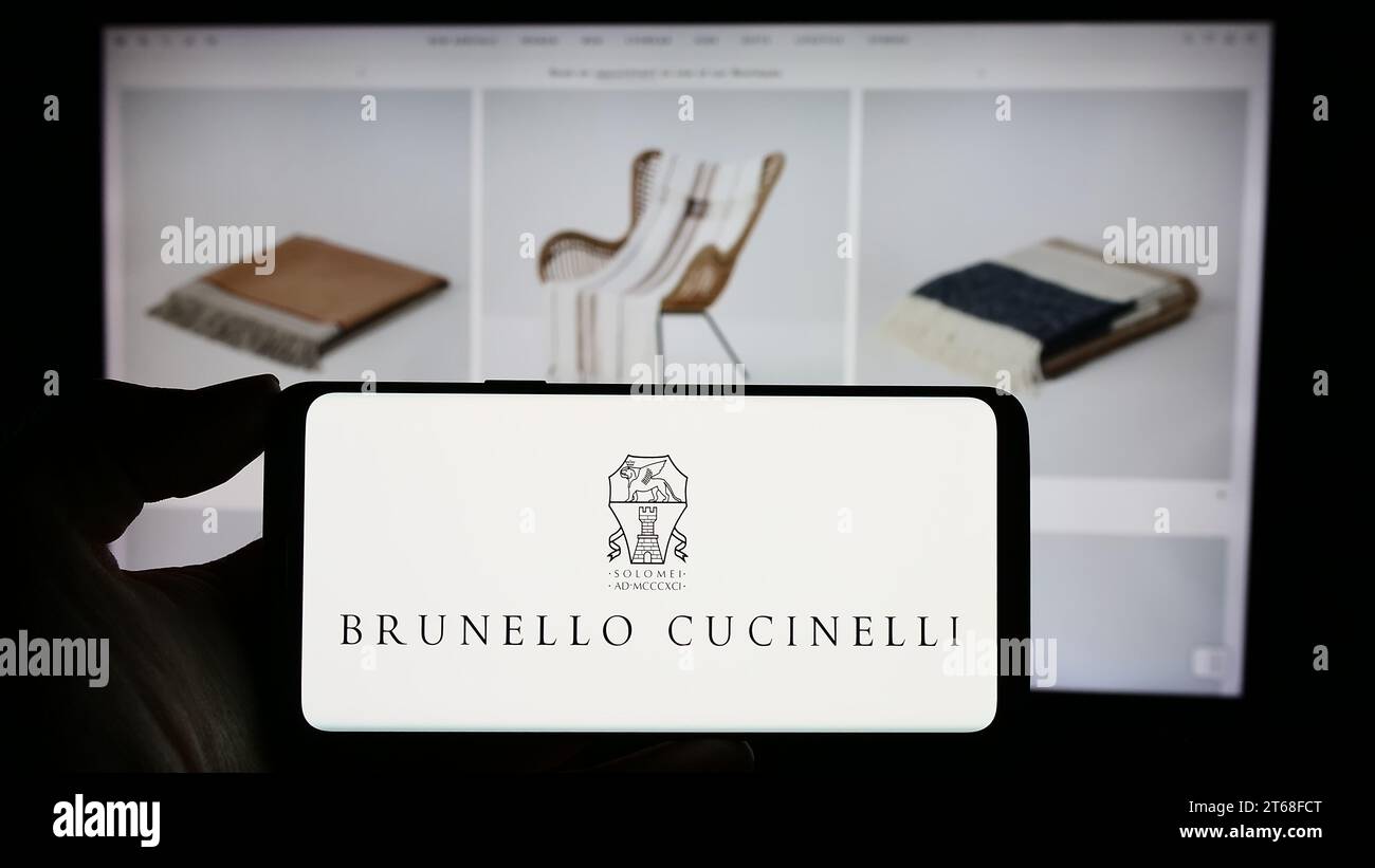 Person holding mobile phone with logo of Italian fashion company Brunello Cucinelli SpA in front of business web page. Focus on phone display. Stock Photo