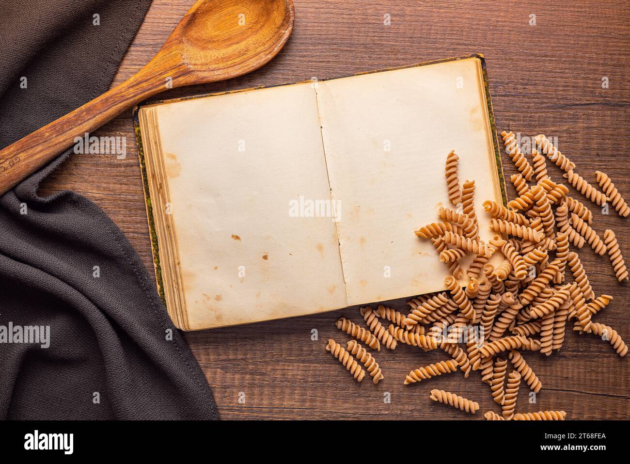 Open blank recipe book and raw whole grain fusilli pasta on the wooden table. Top view. Stock Photo