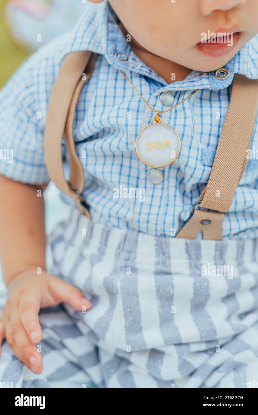 A young infant male baby wearing blue suspenders while sitting down Stock Photo
