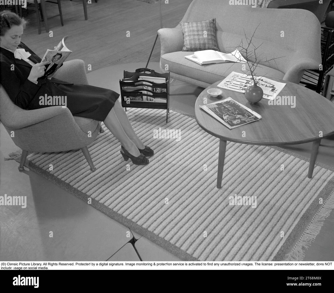 In the 1950s. A woman sitting comfortably in an armchair in a furniture exhibition of typical 1950s furniture at the department store NK in StockholmSweden 1953. Conard ref 2318 Stock Photo