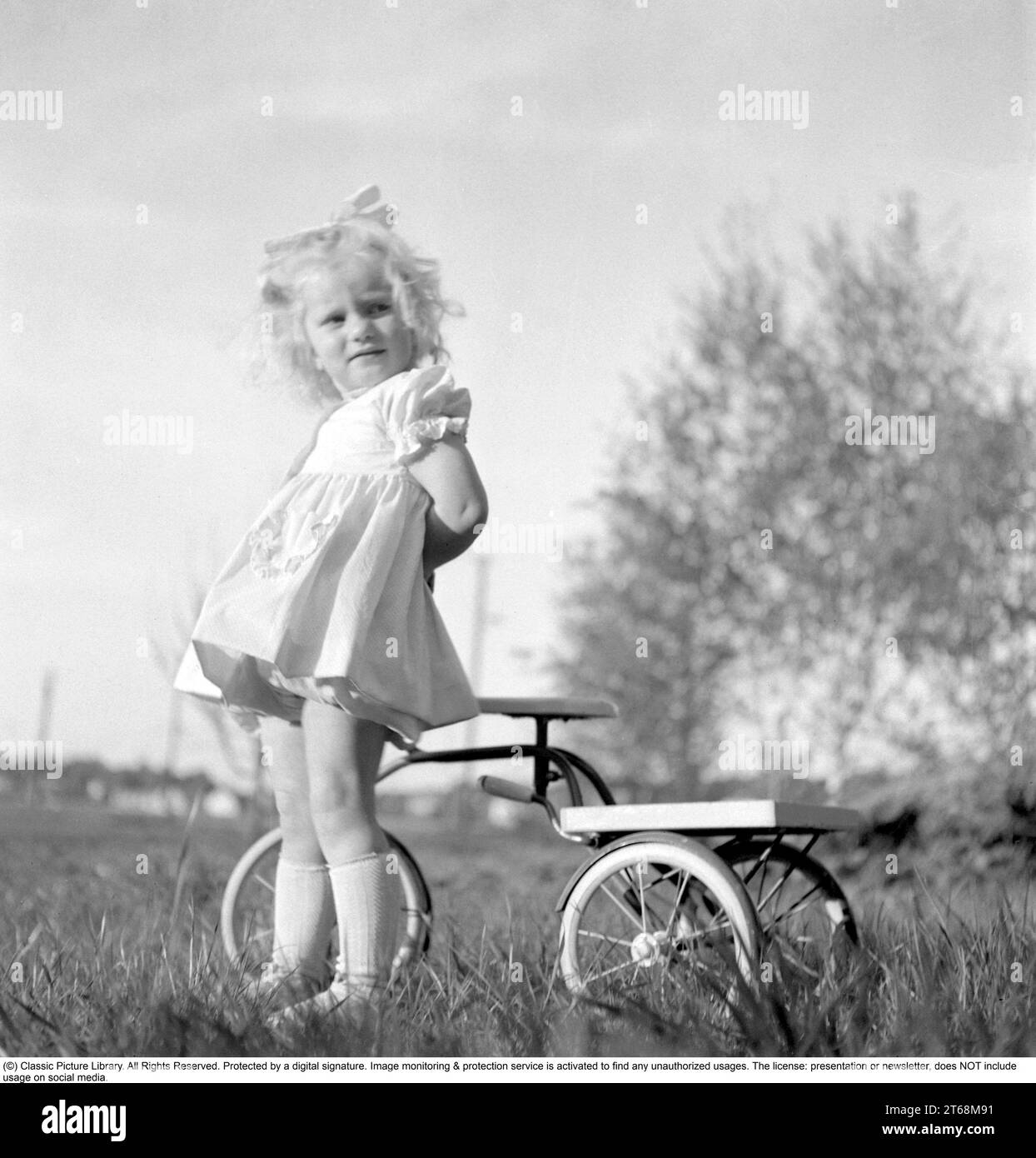 In the 1940s. A blonde little girl in a nice dress on her tricycle. Sweden 1949. Conard ref 1118 Stock Photo