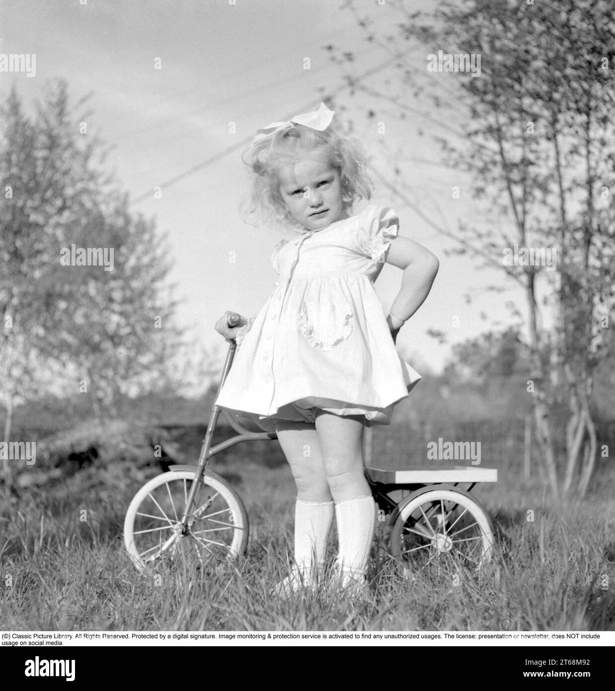In the 1940s. A blonde little girl in a nice dress on her tricycle. Sweden 1949. Conard ref 1118 Stock Photo