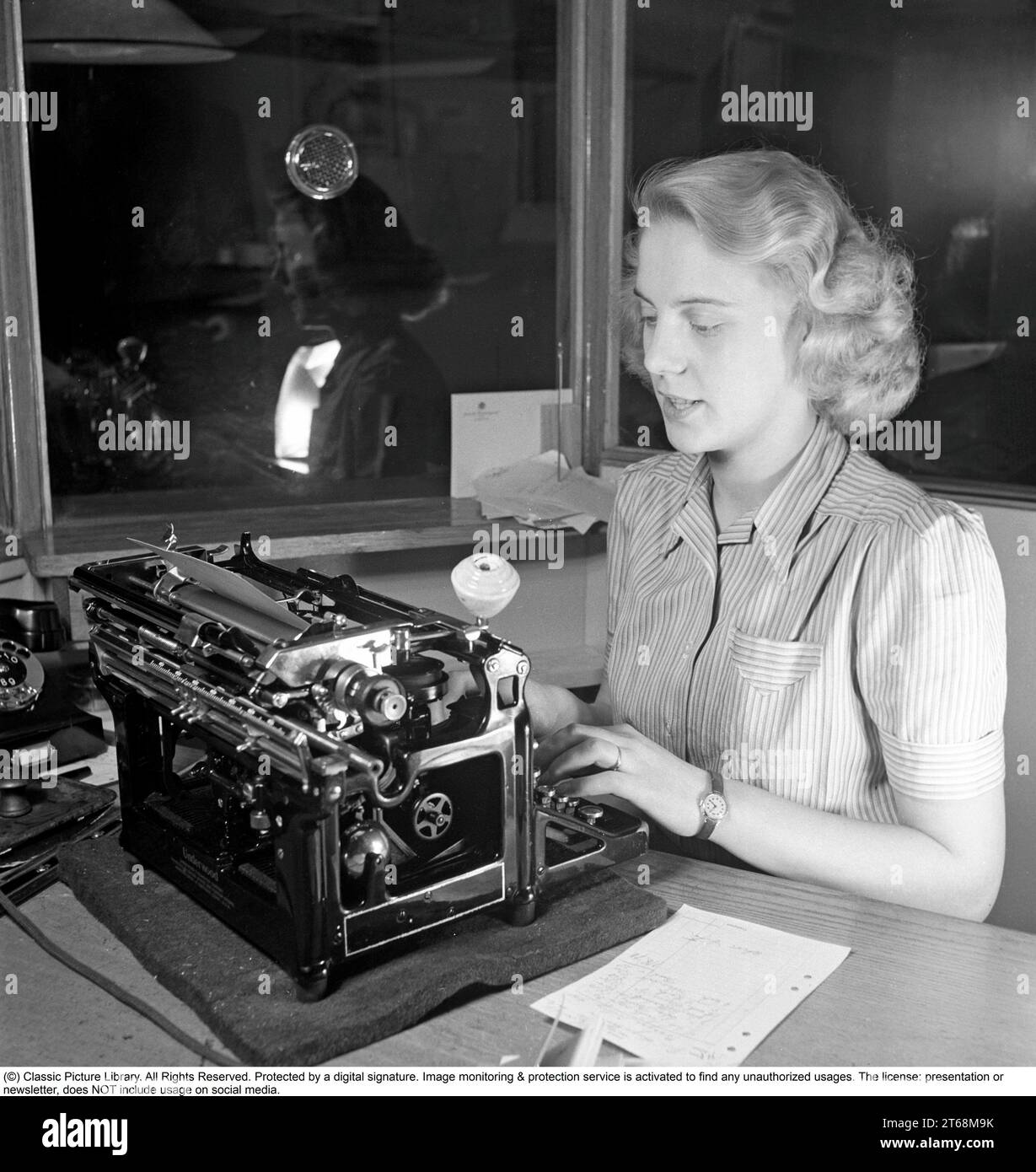 Office girl in the 1940s. A woman is sitting at a office desk typing on her typewrite. Sweden 1942. Photo Kristoffersson A130-6 Stock Photo