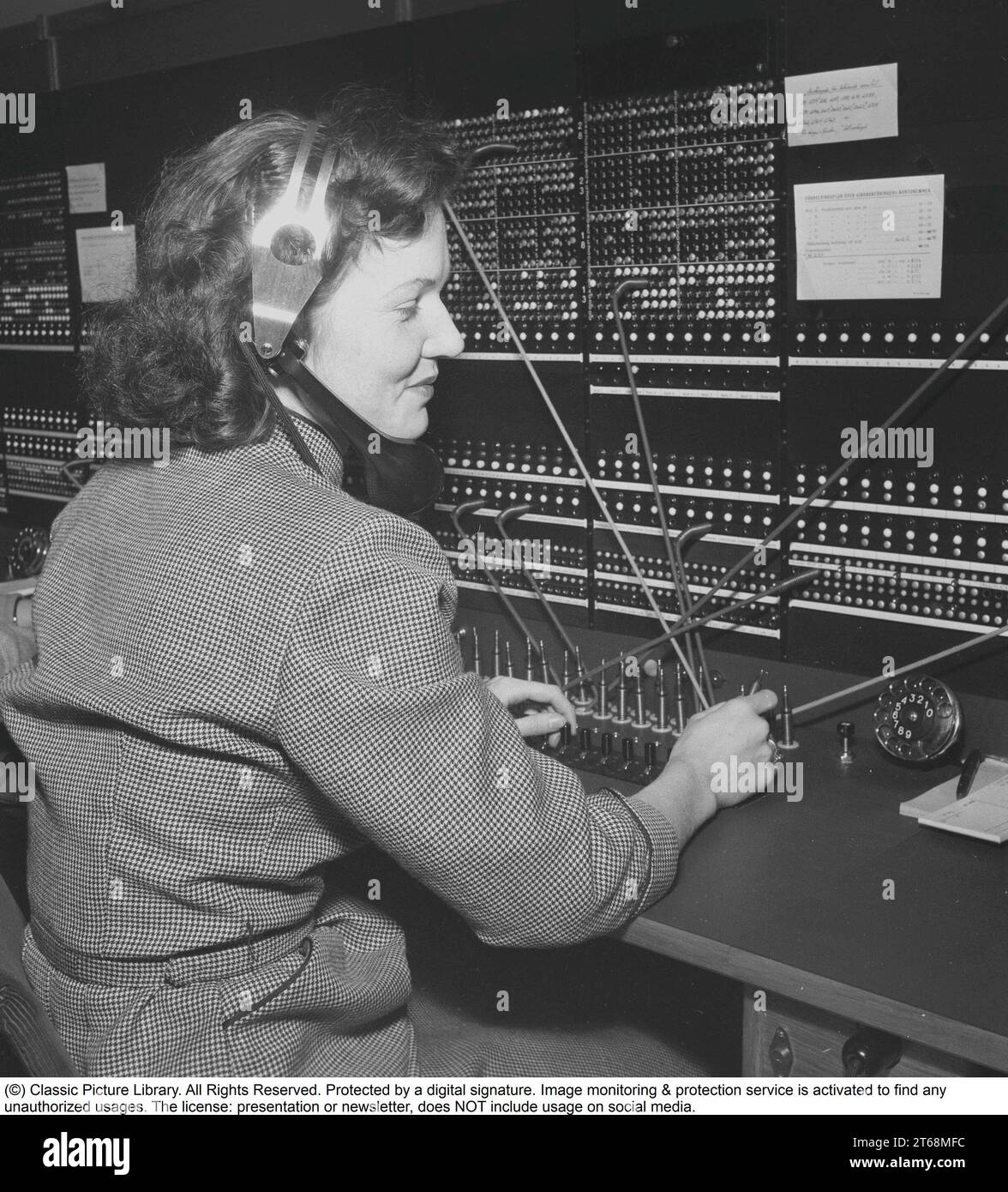 Telephony in the 1950s. Woman working at a telephone switchboard as it's operatos. A telephone communication system that was manually operated where the incoming calls were forwarded and redirected to the another telephone number by the operator, in this case locally within the building serving a company or an organization with many internal telephone lines. The switchboard operator could take messages, put you on hold if the line was busy. Sweden 1953. Kristoffersson ref BM99-7 Stock Photo