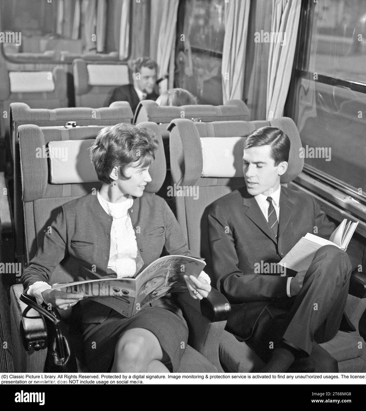 Train travel in the 1960s. A couple on a train, sitting comfortably in the carriage reading a magazine and a book. Sweden 1960s Kristoffersson ref DD118-11 Stock Photo