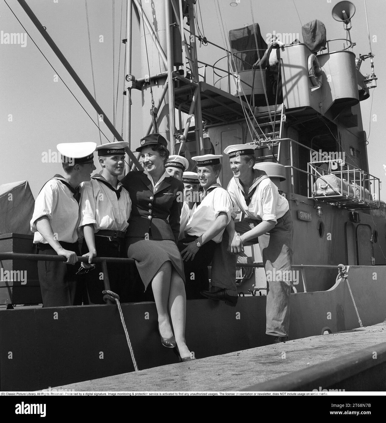 In the 1950s. A young woman in uniform at the dock surrounded by sailors from the crew of the ship Sturkö, which belongs to the Swedish Navy. The picture was taken in Visby on the island of Gotland, Sweden in 1959. Kristoffersson ref CG40-5 Stock Photo