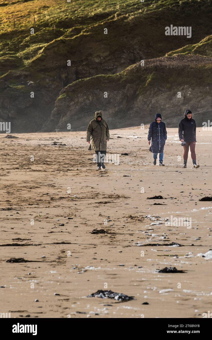 Three people walking on Holywell Beach in Cornwall in the UK. Stock Photo