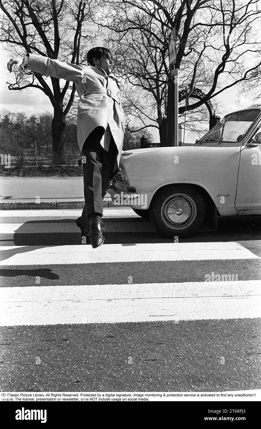 In the 1960s. A moment when a man walks on a pedestrian crossing but a car has not noticed him and keeps driving. The man jumps away from the car to avoid being hit by it. Sweden 1968. Kristoffersson ref 3-57 Stock Photo