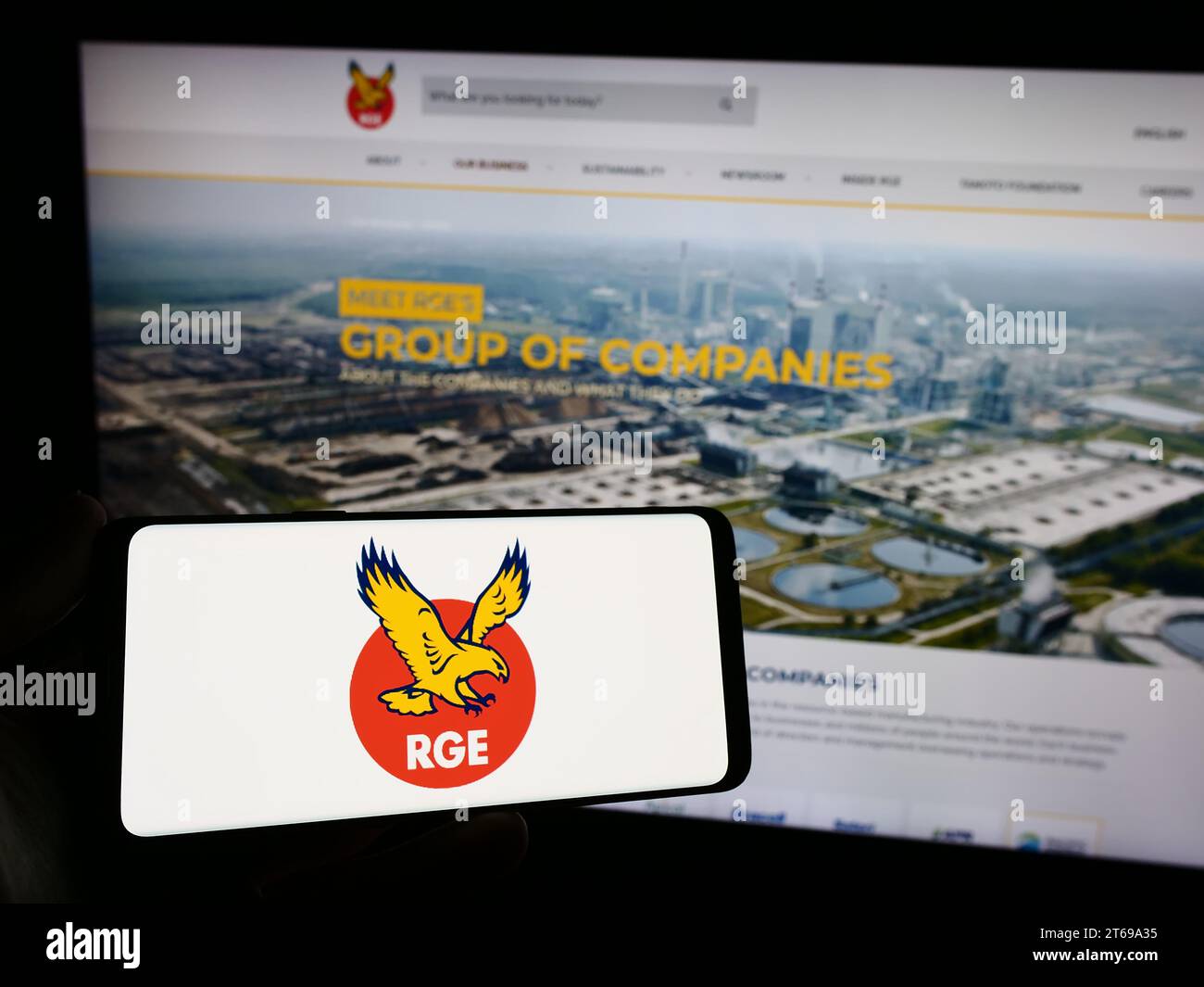 Person holding smartphone with logo of Singaporean company Royal Golden Eagle (RGE) in front of website. Focus on phone display. Stock Photo