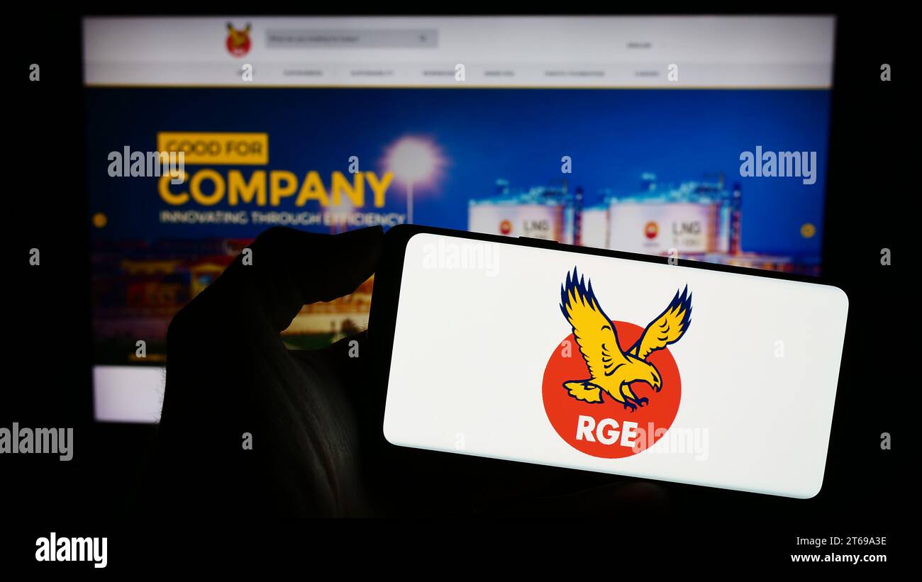 Person holding mobile phone with logo of Singaporean company Royal Golden Eagle (RGE) in front of business web page. Focus on phone display. Stock Photo