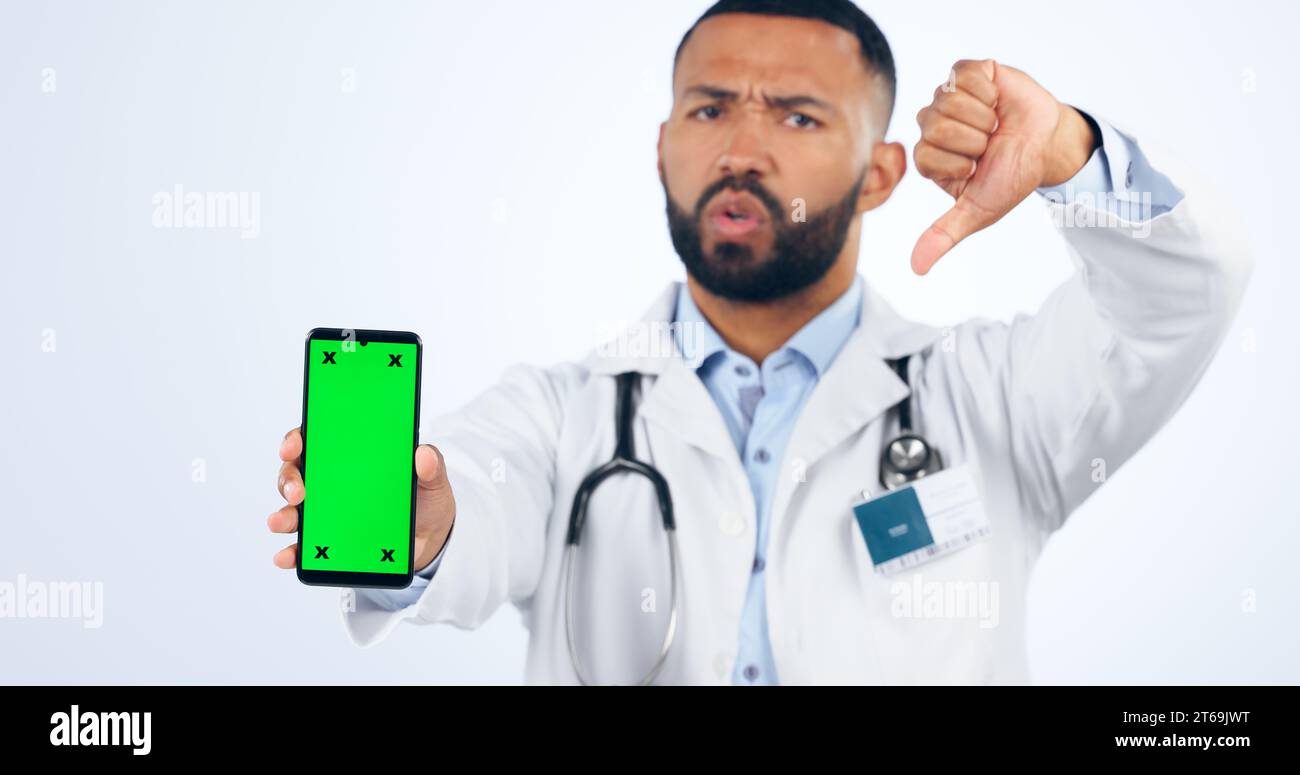 Phone, green screen and portrait of doctor with thumbs down, review or fake news in white background. Studio, healthcare or sign for negative Stock Photo