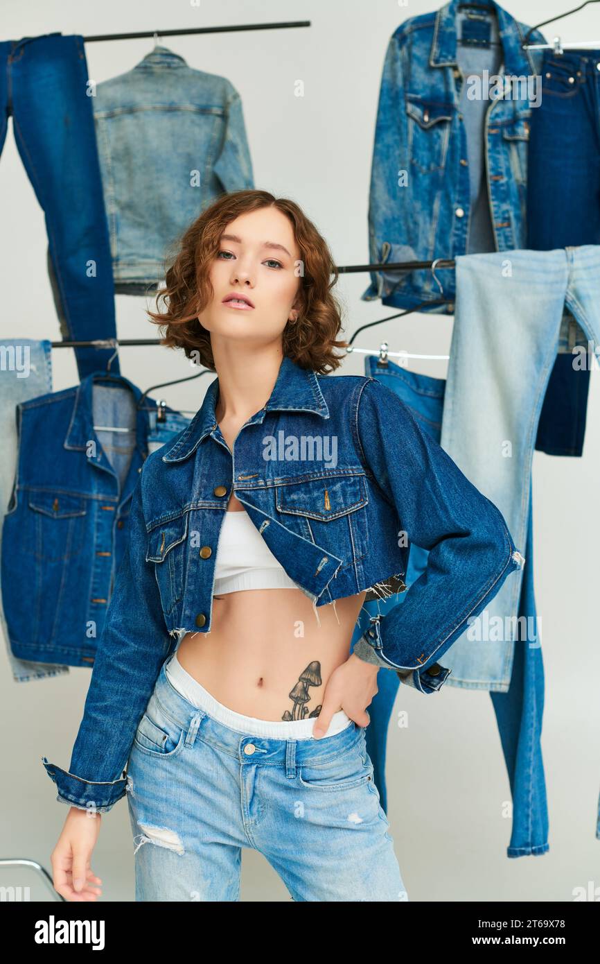 stylish gen z model in cropped jacket and jeans posing among denim clothes on gray background Stock Photo Alamy