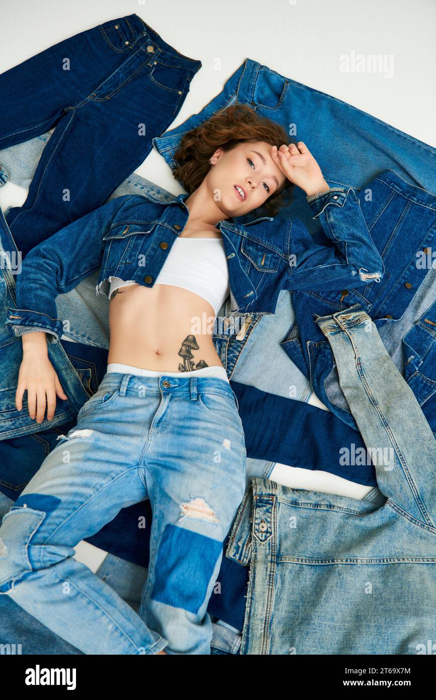 top view of stylish young model lying on pile of different denim clothes, fast fashion concept Stock Photo