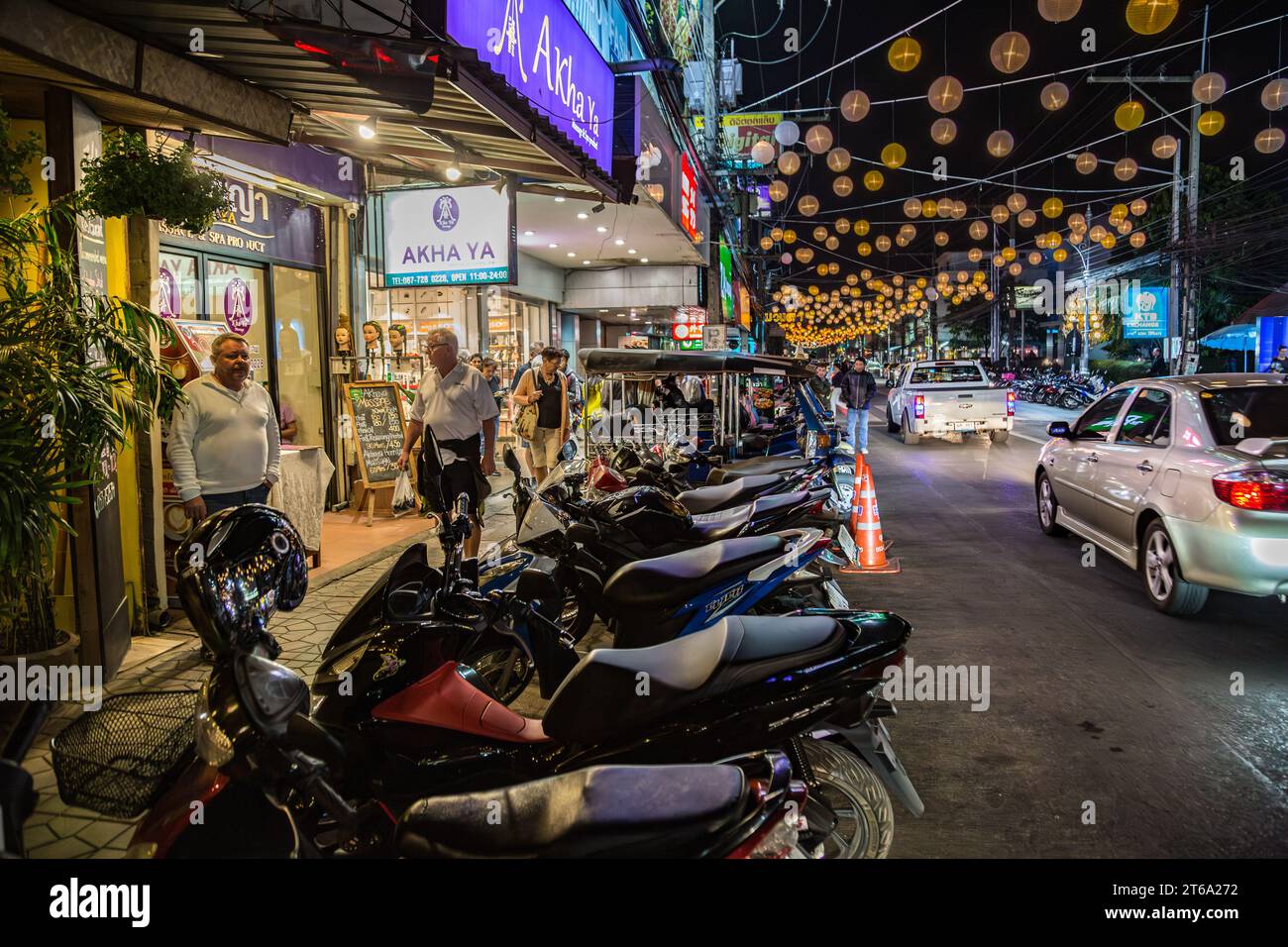 Motor scooters line the side of the downtown street in Chiang Rai ...