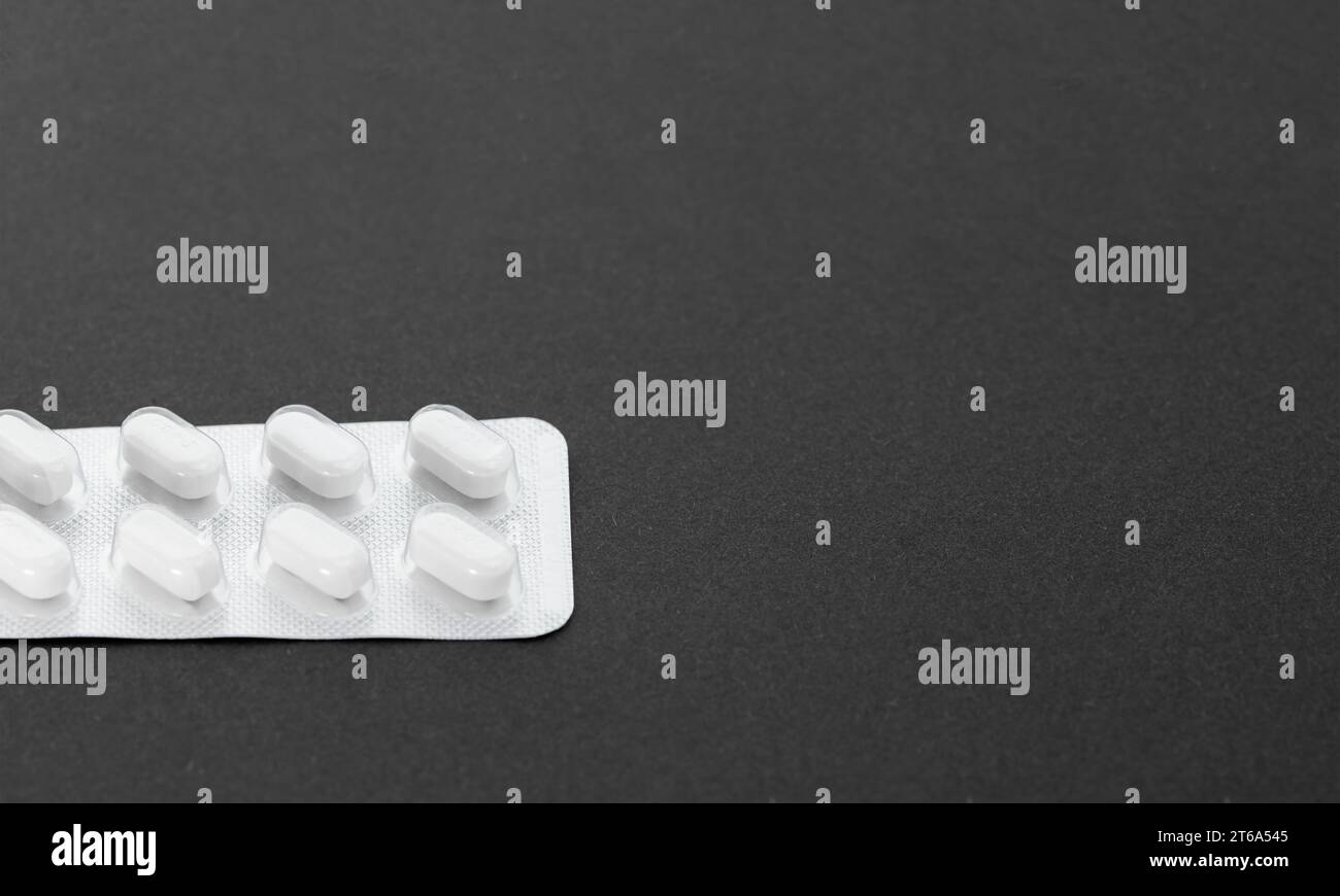 Part of blister pack with white pills on black textured background. Stock Photo