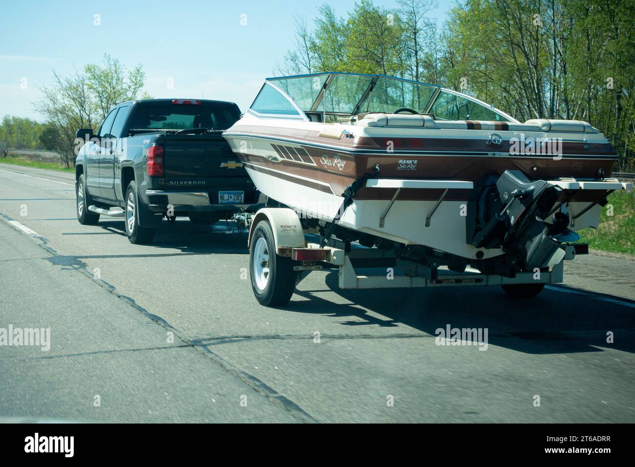 Green Chevy Silverado towing a classic Hank's Sea Ray Seville's speed boat with a powerful inboard motor on the highway. Nisswa Minnesota MN USA Stock Photo