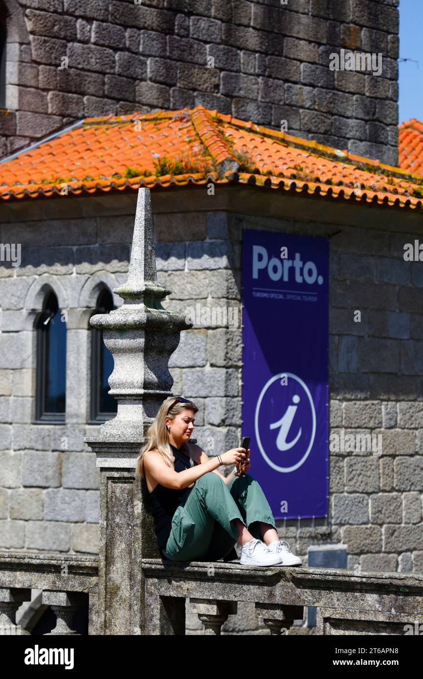 A female tourist looks at her smartphone in front of the Porto Tourism Association office