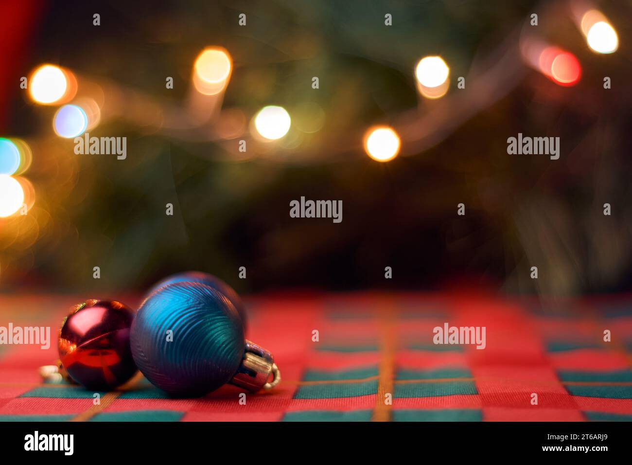 Horizontal Christmas background with Christmas balls on table with green and red tablecloth, blurred Christmas tree and lights. Copy space for text. Stock Photo